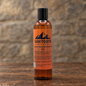 Autumn Mountain Beard Wash in its orange-labeled bottle on rustic wood against a stone backdrop