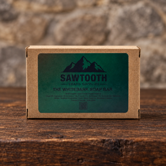 The Whitebark Soap Bar in its dark green-labeled kraft carton on rustic wood against a stone backdrop